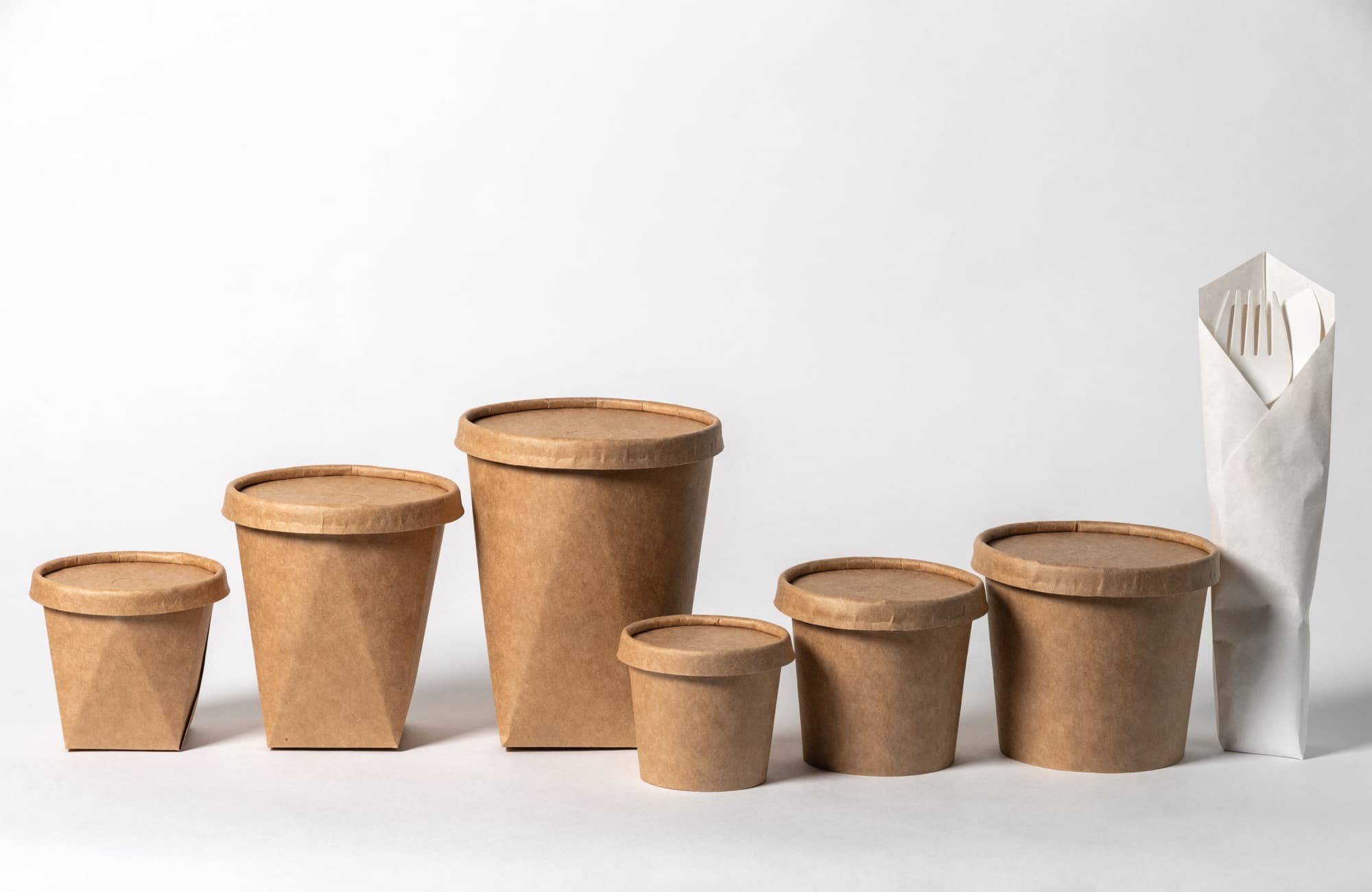 Kraft paper food containers and tubs with lids beside a paper cutlery pouch